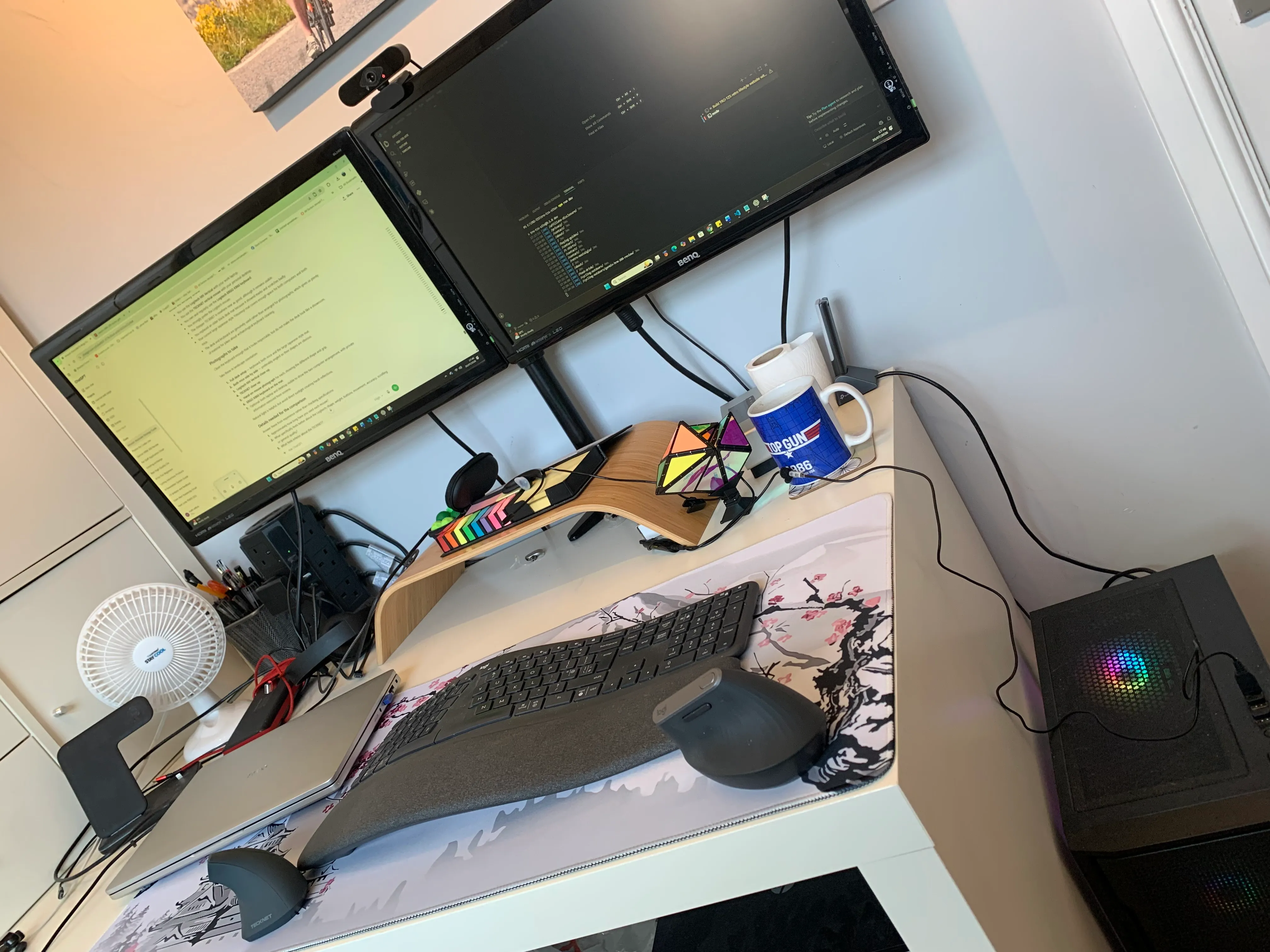 Angled view of a home office desk with two monitors and two computers
