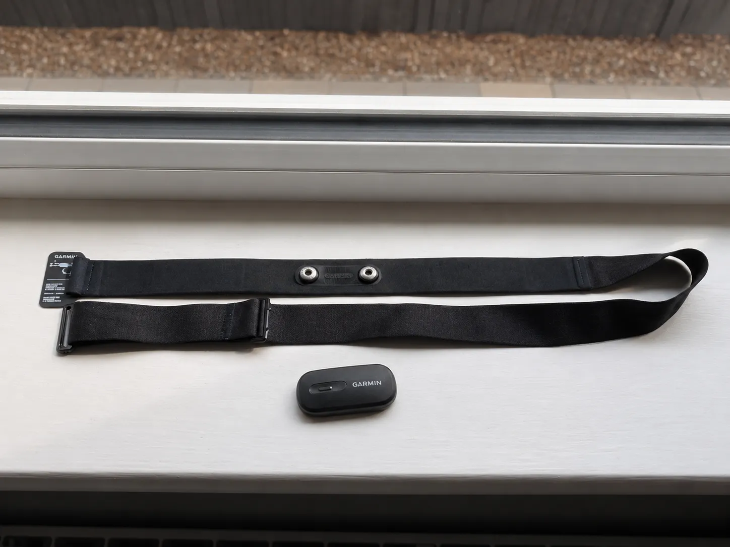 Garmin HRM-200 heart-rate monitor pod beside its black chest strap on a windowsill