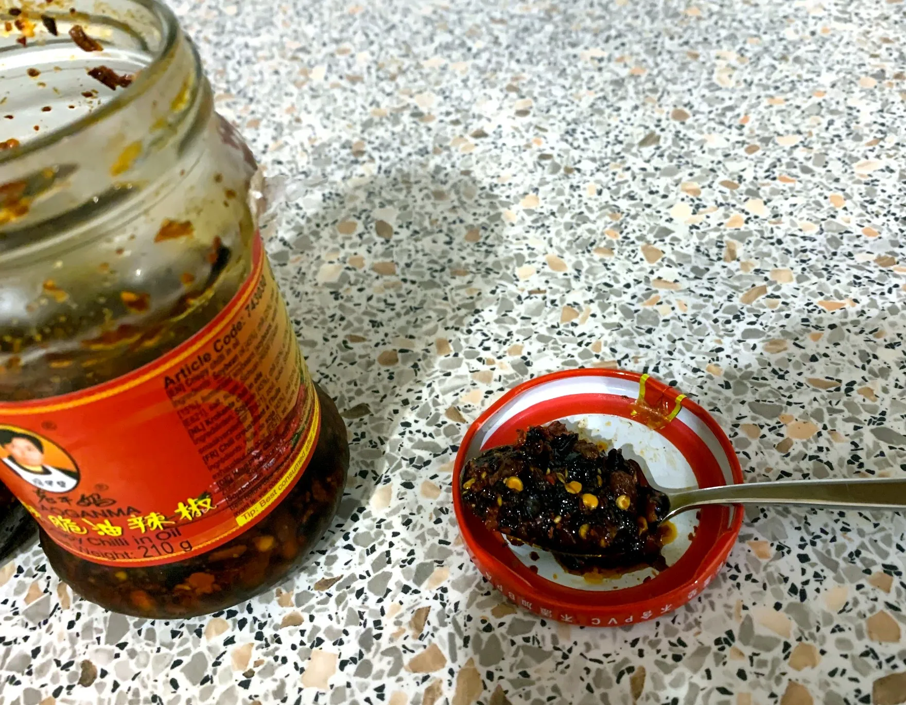 Open jar of Lao Gan Ma crispy chilli oil beside a spoonful showing the chunky texture
